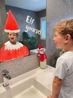 a young boy is looking at the elf in the mirror on the bathroom wall next to the sink