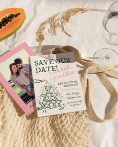 save - the - dates cards and wine glasses are sitting on a tablecloth next to two slices of papaya