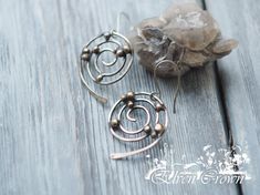 two silver spiral earrings sitting on top of a wooden table next to a rock and crystal