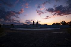 two people standing in the middle of a circle at sunset with clouds and blue sky behind them