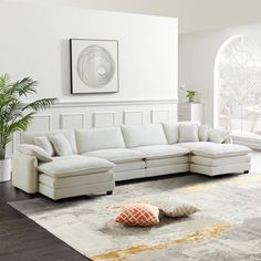 a living room with a large white sectional couch in the center and an orange pillow on the floor