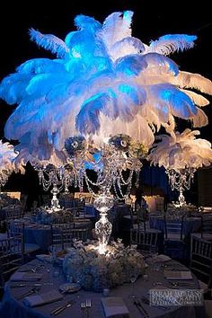 the centerpieces are decorated with blue feathers and crystal beaded chandeliers