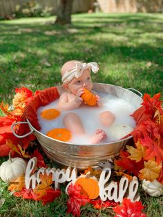 a baby sitting in a metal tub filled with water and oranges on the ground