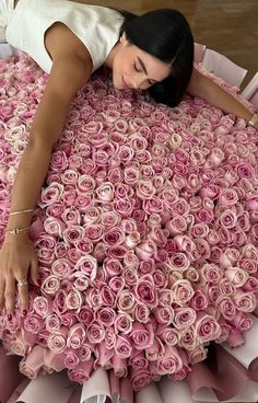 a woman laying on top of a giant pile of pink roses