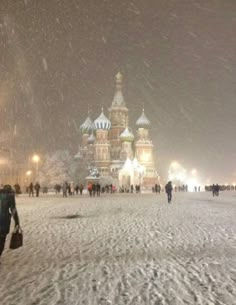 people are walking through the snow in front of an ornate building with many spires