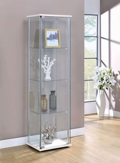 a tall glass display case with silver decorations on the top and bottom shelves, in front of a pink wall