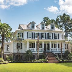 a large white house with black shutters on the front and second story, surrounded by palm trees