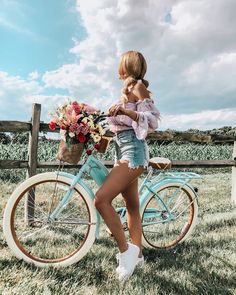 a woman standing next to a blue bike with flowers on the handlebars and holding a basket