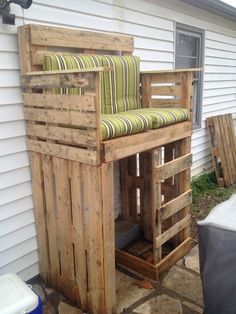 a wooden bench sitting on top of a patio next to a white house with green striped cushions