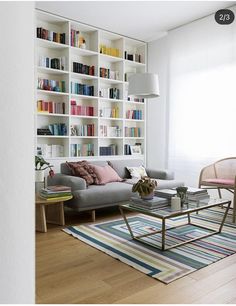 a living room filled with furniture and lots of bookshelves on the wall next to a window