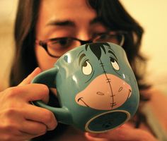 a woman is holding a coffee mug with the face of a cartoon character painted on it