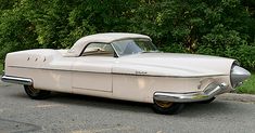 an old car is parked on the side of the road in front of some trees