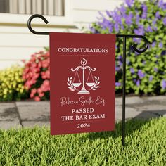 a red sign that says congratulationss placed in the bar exam on grass next to flowers