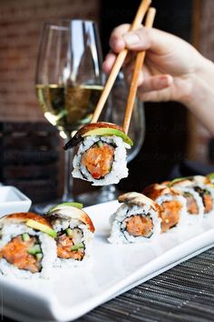 sushi is being served with chopsticks on a white plate next to a glass of wine