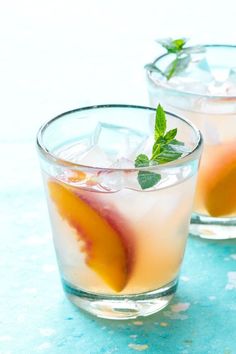 two glasses filled with fruit and ice on top of a blue countertop next to each other