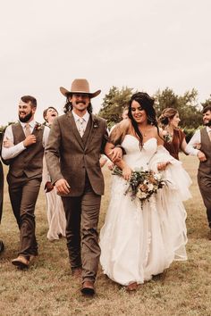 a bride and groom walking through a field with their bridal party in the background