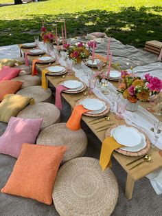 an outdoor table set with place settings and flowers on the plates, napkins, and candles