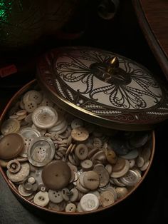 a box filled with lots of buttons on top of a wooden table next to a vase