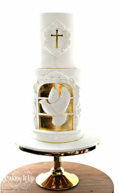 a white and gold wedding cake with a cross on the top is sitting on a stand