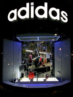 the adidas store is lit up at night with its logo reflected in the window