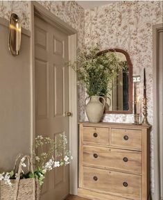 a wooden dresser sitting next to a mirror on top of a wall with flowers in it