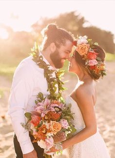 a bride and groom standing on the beach with flowers in their hair