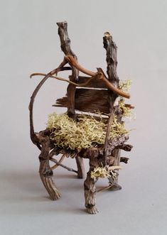 a miniature chair made out of branches and wood with moss growing on the backrest