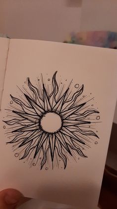 a person holding up a piece of paper with a drawing on it that looks like a sunburst