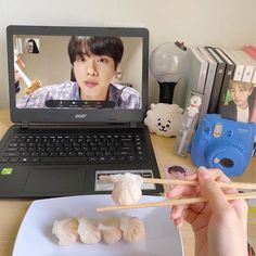 a person is eating food with chopsticks in front of a laptop on a desk