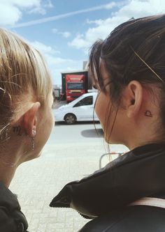 two women are facing each other in front of a parking lot with cars parked on the street