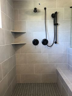 a walk in shower sitting next to a white tiled wall with black faucets