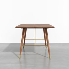 a wooden table sitting on top of a cement floor next to a white wall with gold legs