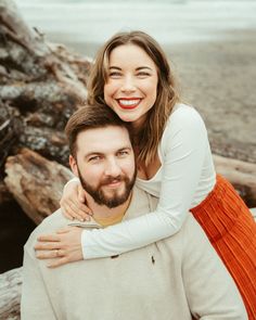 a man and woman hugging each other on the beach with driftwood in the background