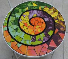 a mosaic table with a spiral design on it's glass top, sitting on a tile floor