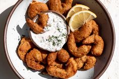 a bowl filled with fried shrimp and dipping sauce next to lemon wedges on a white table