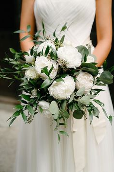 a bridal holding a bouquet of white flowers and greenery on her wedding day