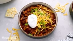 a bowl filled with chili and cheese next to crackers