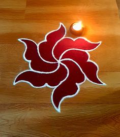 a lit candle sitting on top of a wooden floor next to a red and white flower