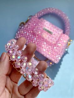 a hand holding a pink purse with lots of beads on it and a small bag in the background