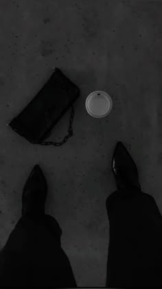 a person standing next to a black purse and a white plate on the ground with their feet up