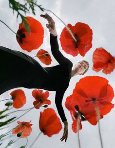 a woman standing in the middle of red flowers with her arms up and hands out