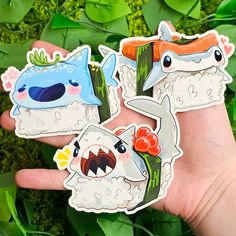 two hand holding three stickers with different designs on them, one has a shark and the other is a fish