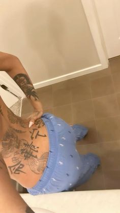 a man with tattoos on his back sitting on the floor in front of a toilet