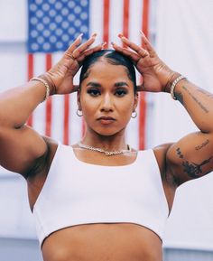 a woman with tattoos on her arms and chest posing in front of an american flag