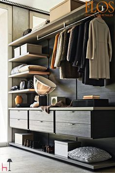 an open closet with clothes and shoes hanging on the shelves, next to a bed