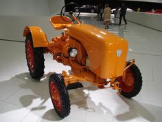 an orange tractor sitting on top of a white tile floor next to people in the background