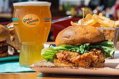 a chicken sandwich with lettuce and tomato on a plate next to a glass of beer