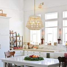 a kitchen with white cabinets and wooden chairs in front of a table that has fruit on it