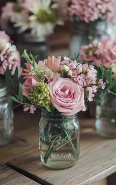 three mason jars filled with pink flowers on top of a wooden table in front of other vases