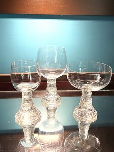 three clear wine glasses sitting on top of a wooden table next to a blue wall